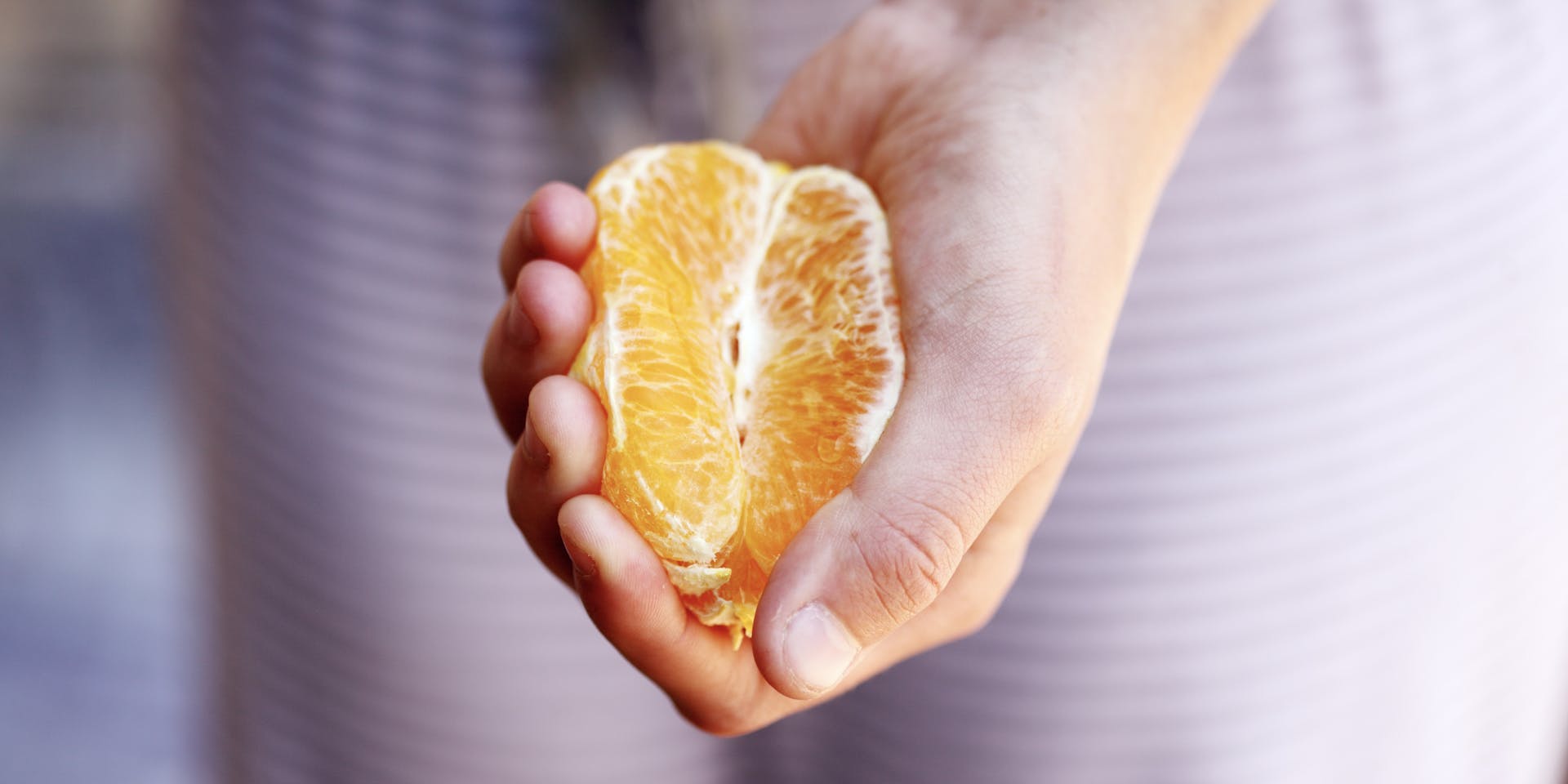 The hand of a white woman, holding half an orange